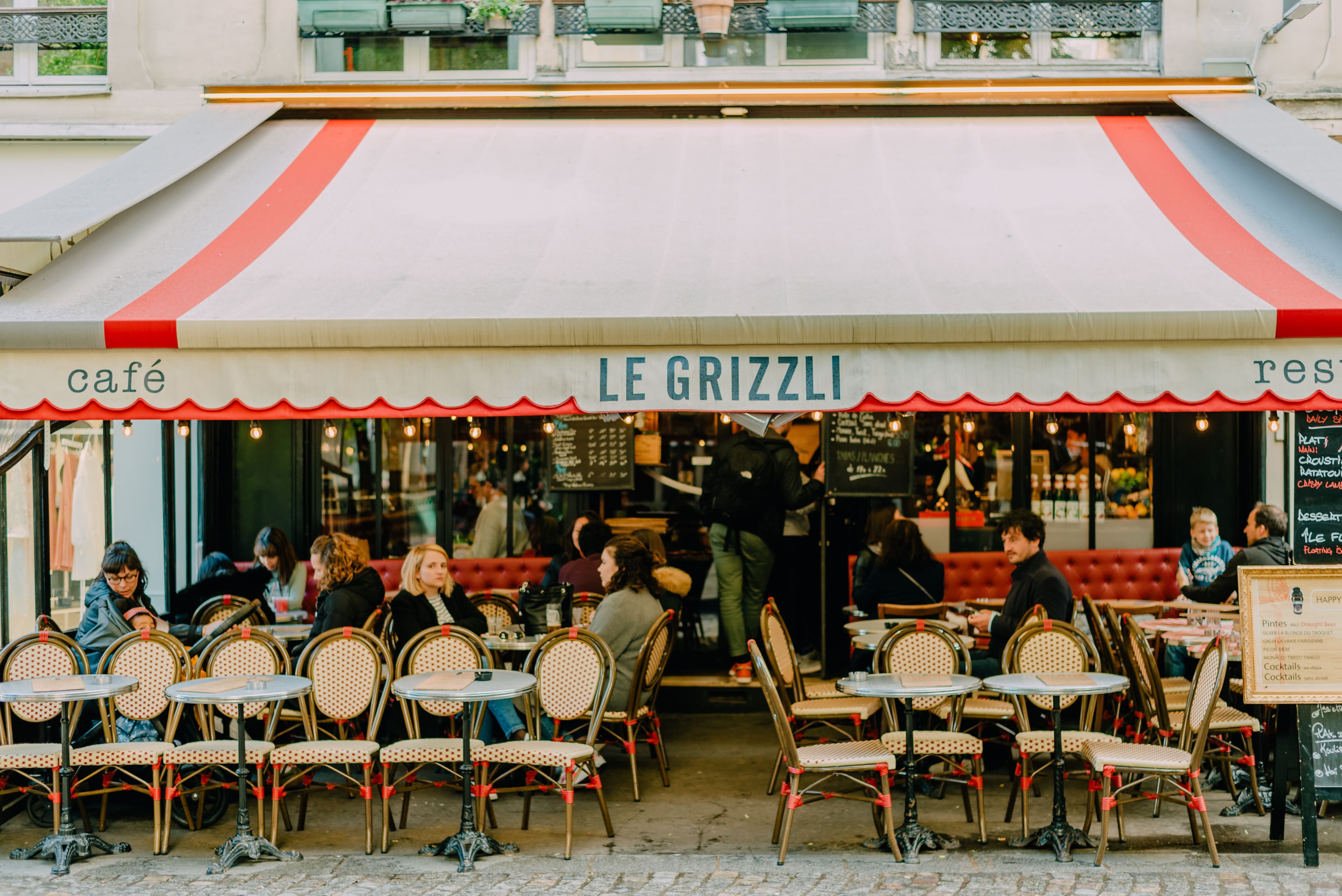 A sunlit café terrace at golden hour, two coffees and a basket of bread on a small round table.