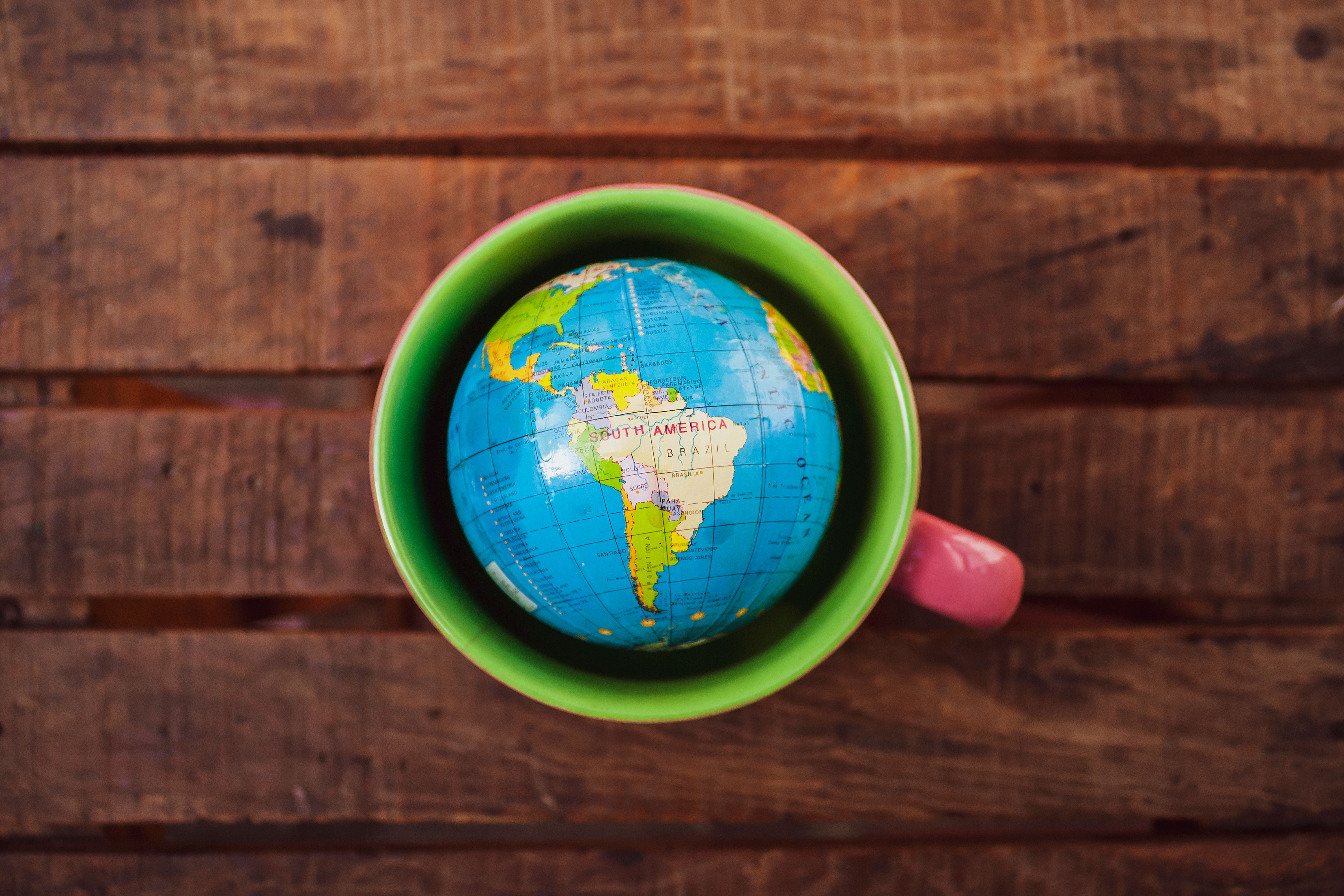 A globe sitting inside a green mug on a wooden table
